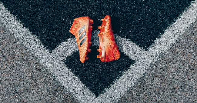 Oranje adidasvoetbalschoenen op een hoekpunt van een voetbalveld.