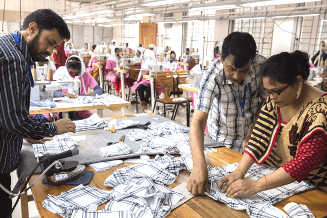Medewerkers in een kledingfabriek staan rondom een tafel met stoffen.